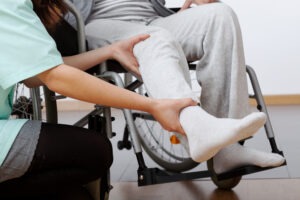 An injured person in a wheelchair, a nurse holds their ankle and knee