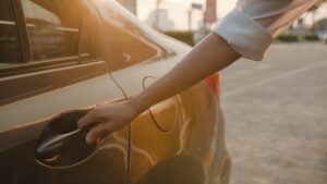A woman reaches to open the door of a rideshare vehicle.