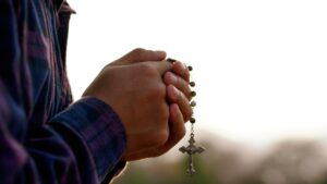 A man holds a rosary in his hands and prays, and wonders who to sue for sexual abuse in the Catholic Church.