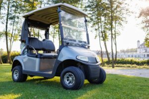 Golf cart parked on grass near a paved path, with a large building in the background